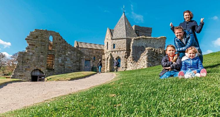 Familia sentada en el césped frente a ruinas medievales.