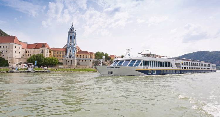 River cruise ship passing by a historic European town alongside a river.