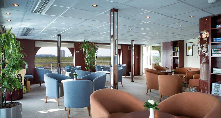 Salon spacieux avec des fauteuils bleu clair et bruns sur un navire de croisière.