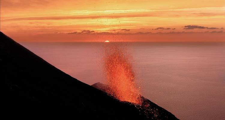 A volcanic eruption with bright orange lava spewing against a sunset sky.