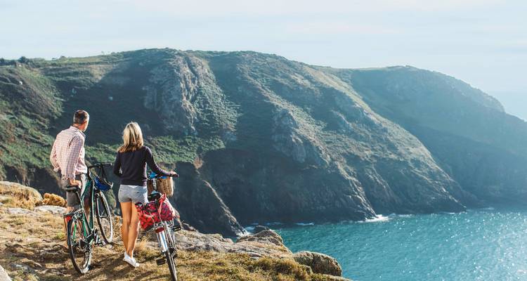Deux cyclistes regardant une falaise maritime et une vue sur l'océan.