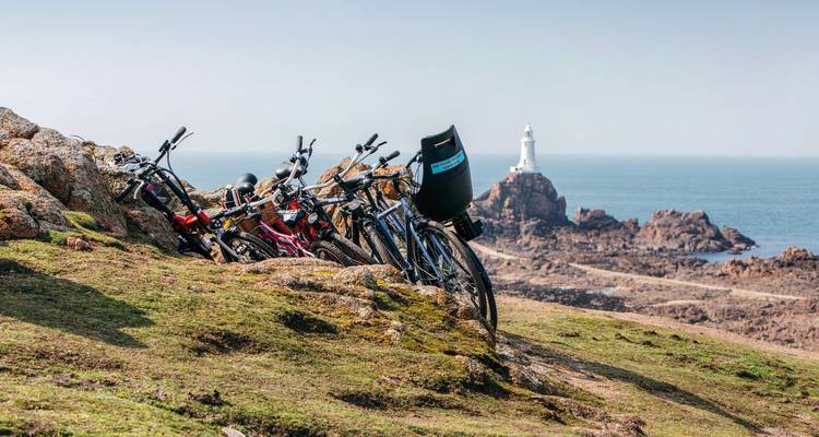 Vélos garés sur un paysage rocheux avec un phare au loin.
