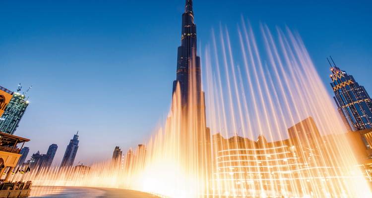 Springbrunnenanlage vor einem hoch aufragenden Wolkenkratzer, nachts beleuchtet.