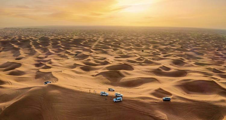 Eine atemberaubende Luftaufnahme von Wüstendünen mit Fahrzeugen bei Sonnenuntergang.