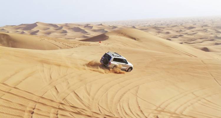 Ein Geländewagen, der durch Sanddünen in der Wüste fährt.