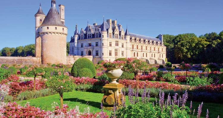 Château surrounded by manicured gardens with vibrant flowers.