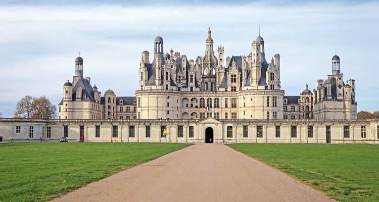 Château with ornate architecture and expansive lawn leading up to it.