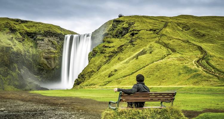 Personne assise sur un banc observant une cascade dans un paysage verdoyant.