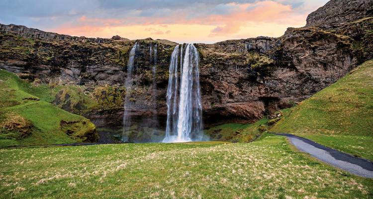 Large waterfall cascading over a cliff with a vibrant sunset sky.