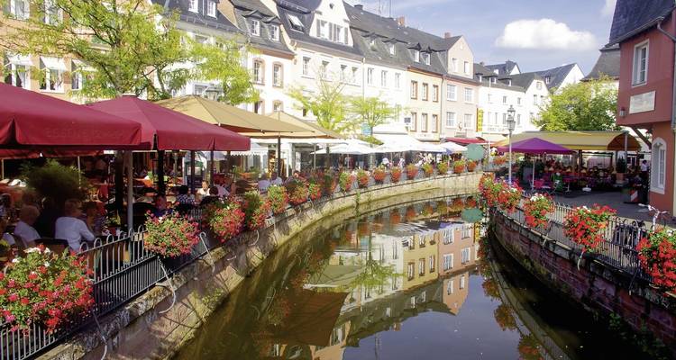 Canal pintoresco con cafés al aire libre y sombrillas rojas.