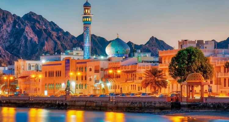 Mosquée avec dôme en mosaïque bleue au coucher du soleil, avec des rues illuminées et des montagnes.
