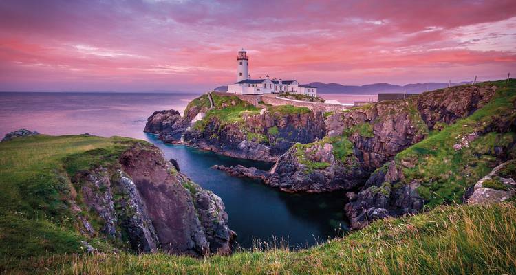Un phare perché sur une falaise au coucher du soleil.