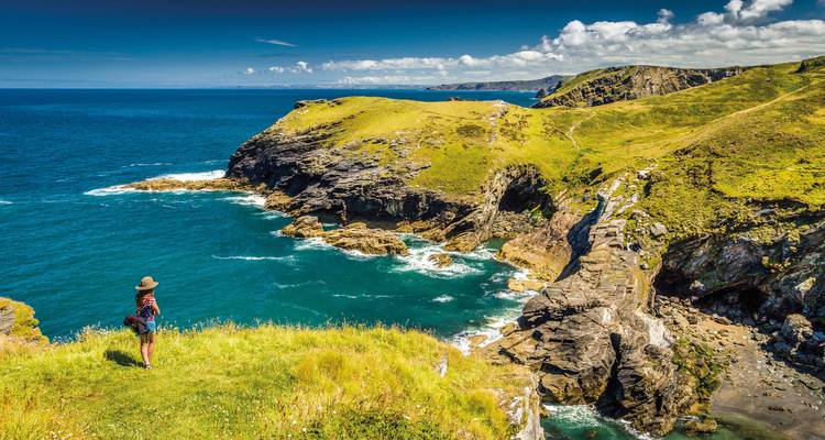Femme debout sur une falaise surplombant un littoral spectaculaire.