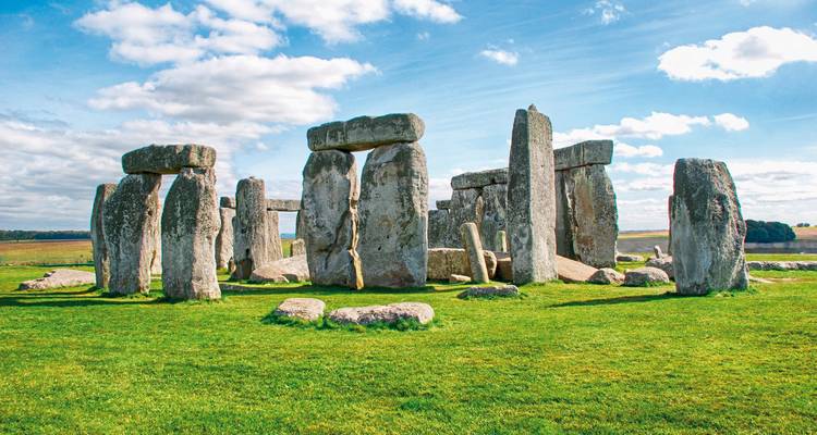 Los megalitos icónicos de Stonehenge se alzan sobre el pasto verde bajo un cielo brillante salpicado de nubes.