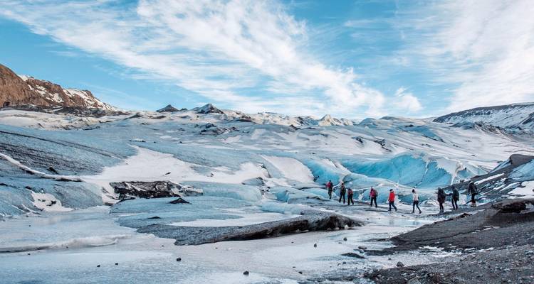 Des randonneurs sur un vaste glacier sous un ciel bleu.
