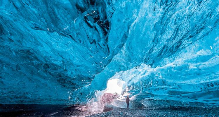 Majestic ice cave interior with a person standing in the entrance.