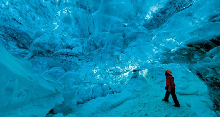 Person walking inside a blue ice cave.