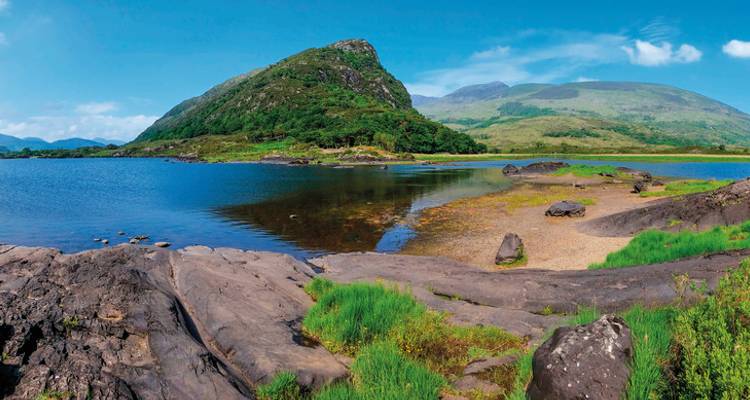 Stunning view of a lake surrounded by lush mountains and clear skies.