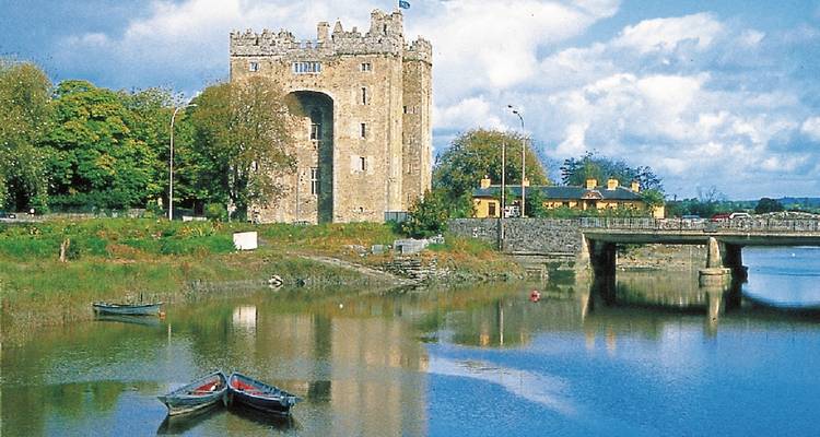 Historic castle by a river with a bridge and boats nearby.
