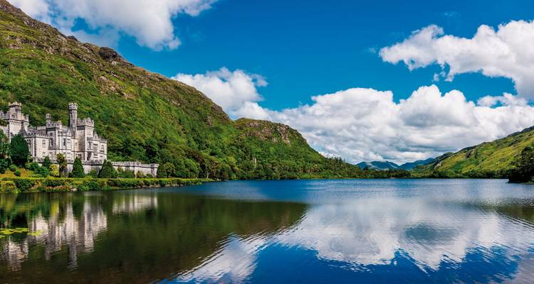 Scenic view of a historic castle by a serene lake, surrounded by mountains.