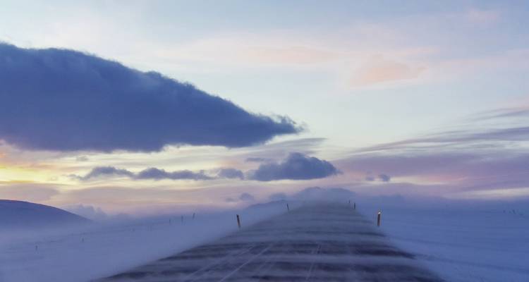 Route enneigée s'étendant au loin avec un ciel coloré.