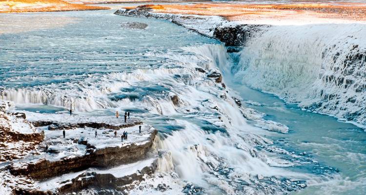 Frozen waterfall with a snowy landscape surrounding it.