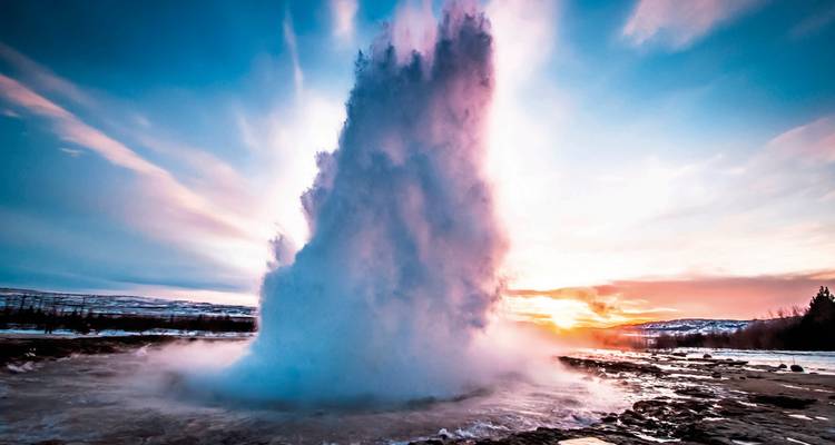 Erupting geyser under a vibrant sky during sunset.