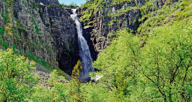 Wasserfall, der eine felsige Klippe hinunterstürzt, umgeben von Grün.