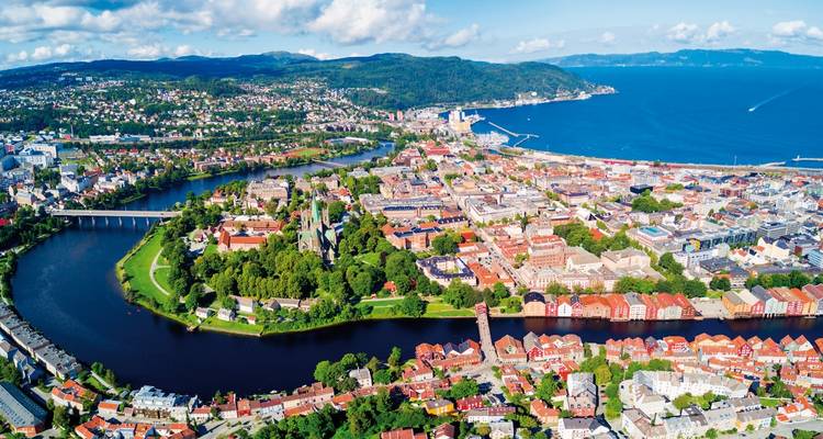 Aerial view of a city with a river, green areas, and structures, likely Trondheim, Norway.