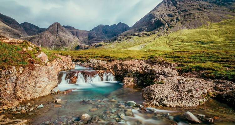 Stream flowing through rocky terrain with mountains in the background.