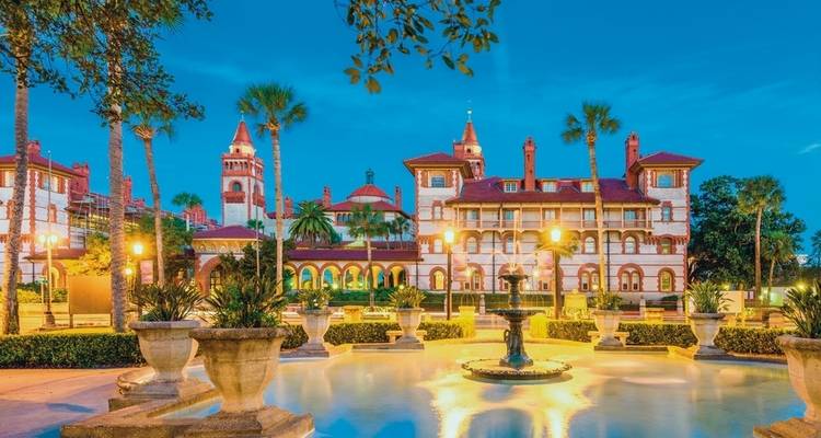 Historic building with palm trees and fountains, beautifully lit at night.