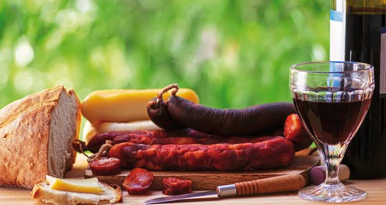 Eine Auswahl traditioneller Speisen mit Würsten, Brot, Käse und Wein auf einem Tisch.