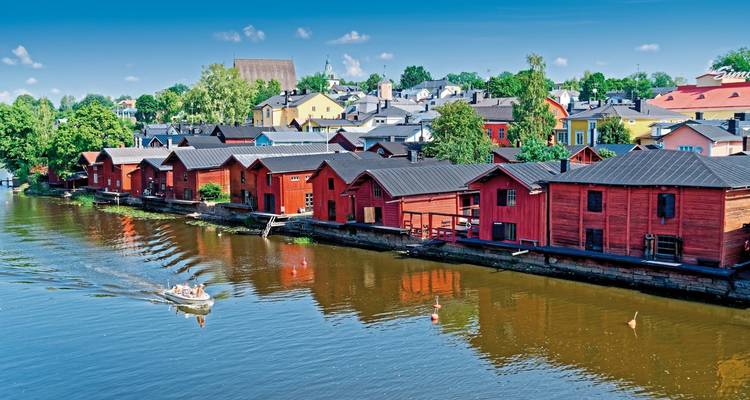 Row of red wooden houses along a river with people in a boat.