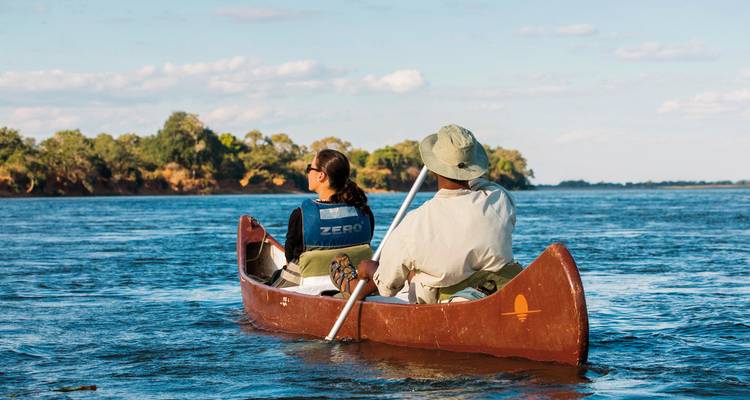 Deux personnes en canoë sur une large rivière, profitant d'une journée ensoleillée.