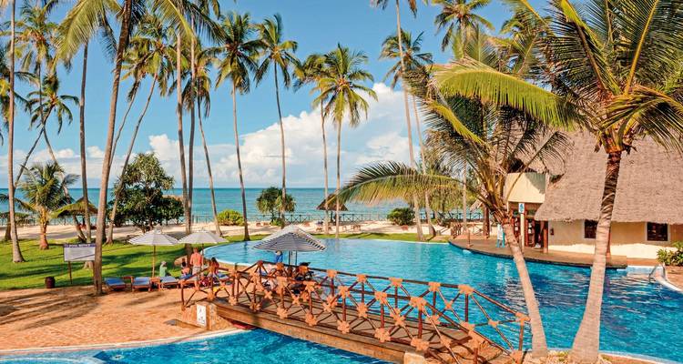 Resort with pool surrounded by palm trees and ocean view.