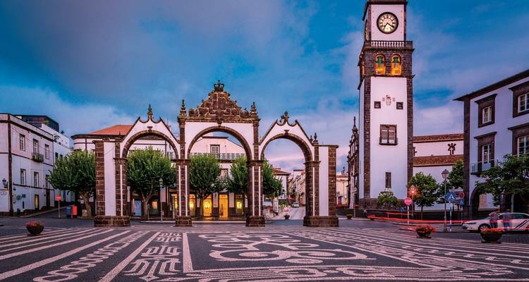 Place de la ville au crépuscule avec des arches ornées et une tour d'horloge.