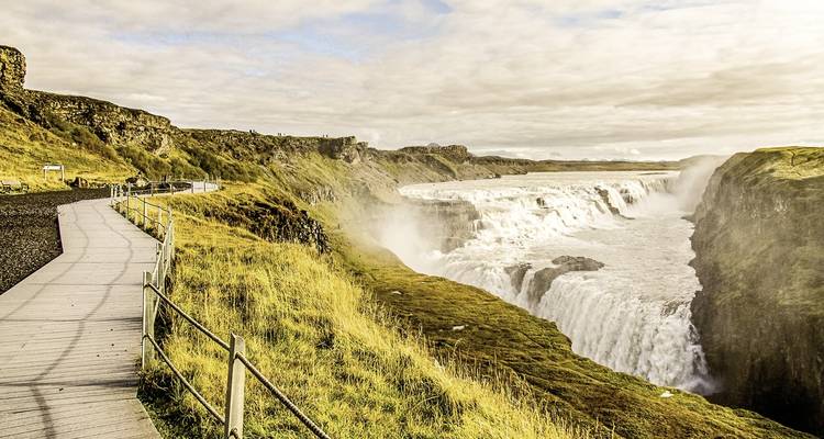 Ein breiter Wasserfall mit schneebedeckten Ufern und einem bewölkten Himmel.