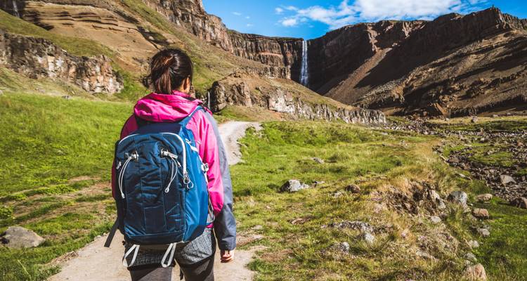 Person hiking on a trail towards a distant waterfall.