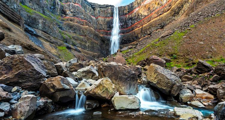A scenic waterfall cascading down a rocky cliff with boulders at the bottom.