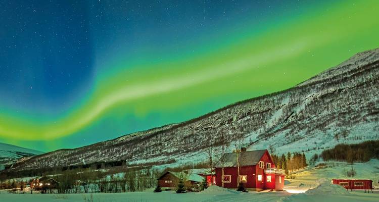Noorderlicht boven een rood huis in een besneeuwde landschap.