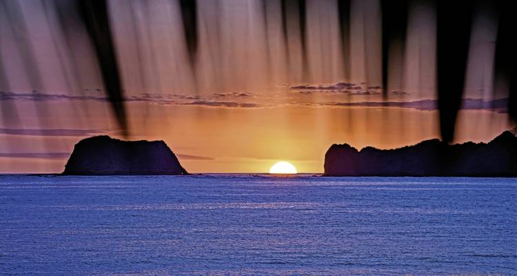 Zonsondergang boven een wateroppervlak met rotsen die zich aftekenen tegen de lucht.