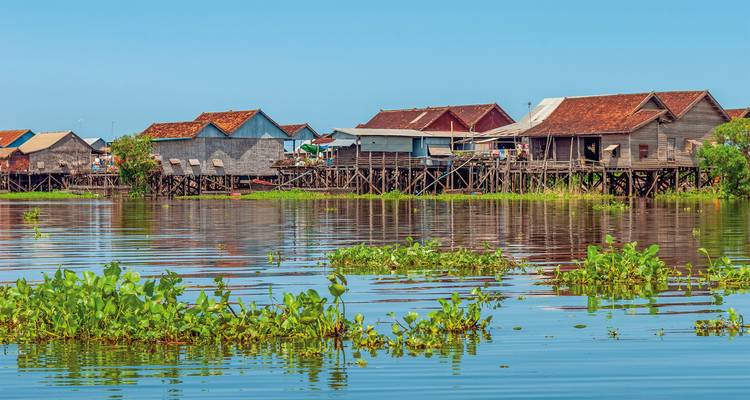 Traditionele paalwoningen op een meer met drijvende groene vegetatie.