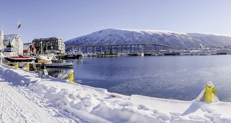 Vue côtière enneigée avec bateaux, pont et montagne à Tromsø, Norvège.