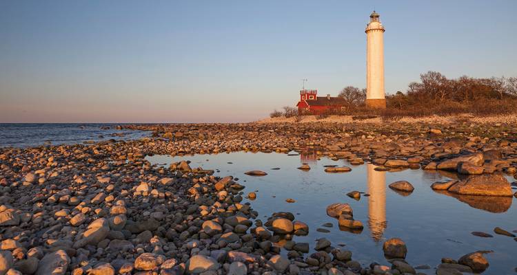 A lighthouse by the sea with rocky shoreline and golden hour lighting.