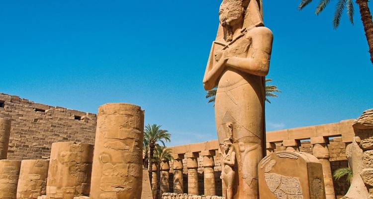 Ancient statue amidst temple ruins with blue sky.