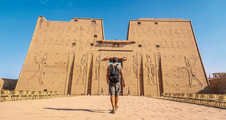 Person walking towards Edfu Temple carved with hieroglyphs.