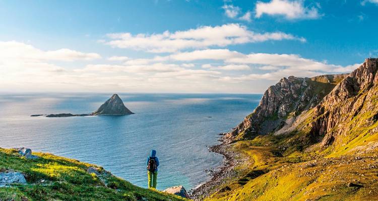 Schilderachtige kustlijn met een wandelaar die uitkijkt over de zee en afgelegen eilanden.