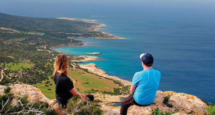 Twee mensen die op een klif zitten en uitkijken over een prachtige kustlijn.