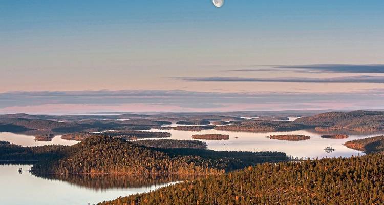 Eine weite Landschaft aus Seen und Wäldern unter einem mondscheinerhellten Himmel.