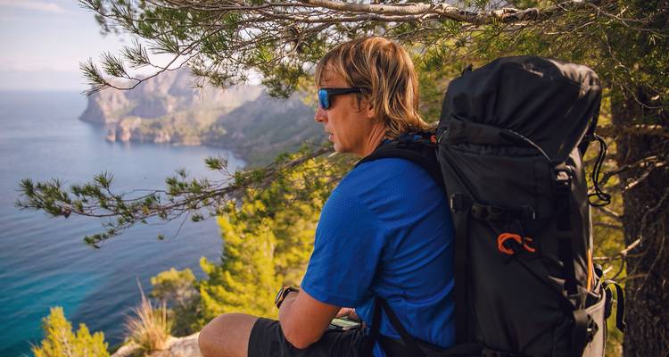 A hiker resting and admiring a coastal view from a hill.